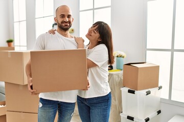 Wall Mural - Young hispanic couple smiling happy holding cardboard box at new home.