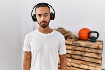 Poster - African american man listening to music using headphones at the gym relaxed with serious expression on face. simple and natural looking at the camera.