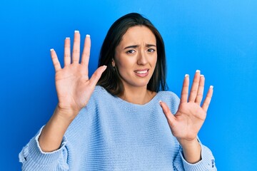 Sticker - Young hispanic girl wearing casual clothes afraid and terrified with fear expression stop gesture with hands, shouting in shock. panic concept.