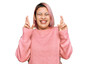 © Krakenimages.com - Hispanic woman with pink hair wearing casual winter sweater gesturing finger crossed smiling with hope and eyes closed. luck and superstitious concept.