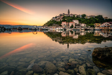 The historical place vrbnik in Croatsia on the island of Krk. In the sunrise directly on the sea, the port, the city is reflected on a rock in the water