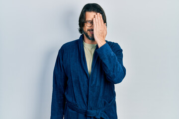 Canvas Print - Middle age caucasian man wearing bathrobe and glasses covering one eye with hand, confident smile on face and surprise emotion.