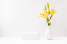 Empty White Box And Yellow Lilies In A Vase On A Light Background. Mockup Banner For Display Of Advertise Product