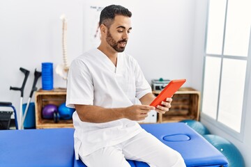 Canvas Print - Young hispanic man wearing physiotherapist uniform having video call at clinic