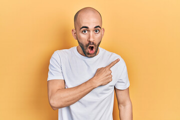 Sticker - Young bald man wearing casual white t shirt surprised pointing with finger to the side, open mouth amazed expression.