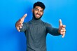 © Krakenimages.com - Arab man with beard wearing turtleneck sweater looking at the camera smiling with open arms for hug. cheerful expression embracing happiness.