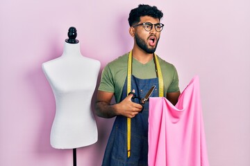 Wall Mural - Arab man with beard dressmaker designer holding scissors and cloth angry and mad screaming frustrated and furious, shouting with anger. rage and aggressive concept.