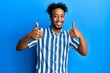 © Krakenimages.com - Young african american man with beard wearing casual striped shirt success sign doing positive gesture with hand, thumbs up smiling and happy. cheerful expression and winner gesture.