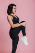 © kalinichenkod - sporty woman stretching her legs and looking at camera on pink background