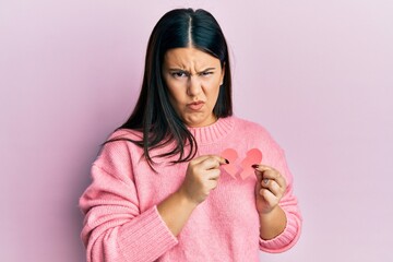 Poster - Beautiful brunette woman holding broken heart paper shape skeptic and nervous, frowning upset because of problem. negative person.