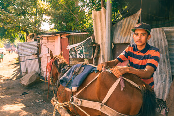 Hispanic poor boy preparing his horse used for product transportation.