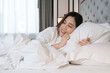 © Avirut S. - Asian woman waking up in her bed, stretching and smiling. Woman lying on the bed in the morning. Asian female sleeping in bed after wake up in the morning. Attractive Asian woman on bed in bedroom.