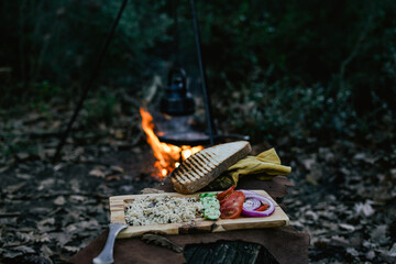 Wall Mural - Campfire spool and salad in pan, water bottle and titanium mug near the fire outdoors. bushcraft, adventure, travel, tourism and camping concept