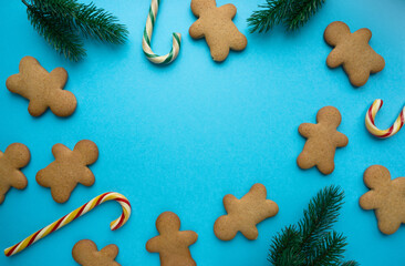 Wall Mural - Christmas gingerbread cookies in the shape of man with lollipops and fir branches on blue background, copyspace