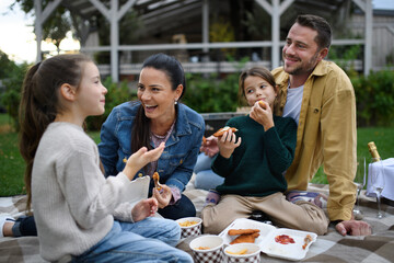 Happy young family sitting on blanket and having take away picnic outdoors in restaurant area.