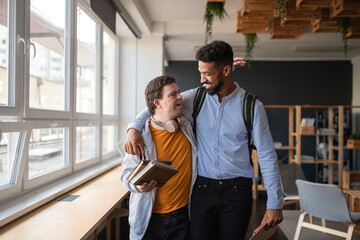 Young man with Down syndrome and his tutor with arms around looking at each other indoors at school