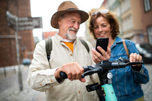 Close Up Of Happy Senior Couple Tourists Scanning Code To Rent A Scooter Together Outdoors In Town