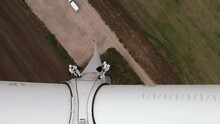 Service Engineers With Safety Harnesses And Long Ropes Go Down Wind Turbine Propeller Tower Above Agricultural Plowed Field Upper View