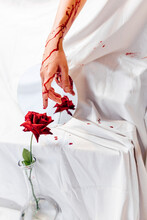 Woman with bloody hand touching red rose in flower vase