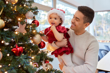 Poster - winter holidays and family concept - happy middle-aged father and baby daughter decorating christmas tree with toy candy cane at home