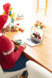 © vectorfusionart - African american woman in santa hat making laptop christmas video call with waving caucasian couple