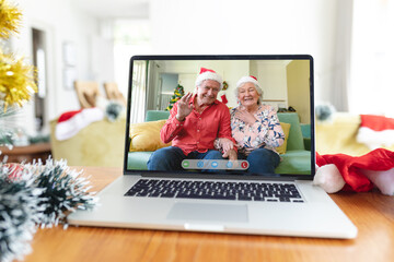 Poster - Happy caucasian senior couple in santa hats smiling on laptop video call screen at christmas time