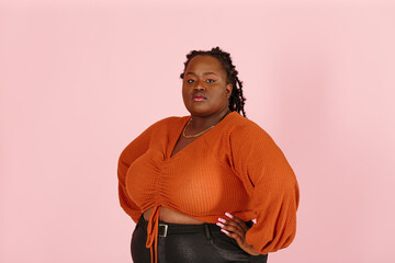 Young confident black plus size body positive woman looks at camera holding hands on waist on light pink background in studio closeup
