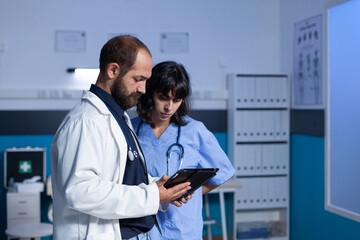 Wall Mural - Doctor and nurse working late at night for healthcare using digital tablet. Medical assistant and medic doing teamwork in cabinet for medicine. Specialists looking at modern device