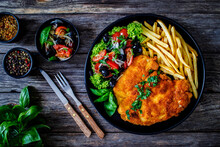 Breaded Fried Pork Chop With French Fries And Fresh Vegetables On Wooden Table
