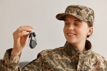 Indoor Shot Of Happy Smiling Woman Soldier Wearing Camouflage Uniform And Hat, Posing At Home, Holding And Looking At Key In Hands, Buying New Flat Or Car.