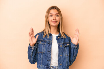 Wall Mural - Young caucasian woman isolated on beige background holding something little with forefingers, smiling and confident.