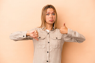 Wall Mural - Young caucasian woman isolated on beige background showing thumbs up and thumbs down, difficult choose concept