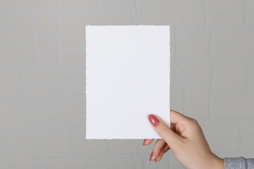 Wall Mural - Woman hands holding blank paper sheet A5 size or letter on grey wall background. Close up of 5x7 ratio card white empty card mockup in female hand, invitation or greeting card