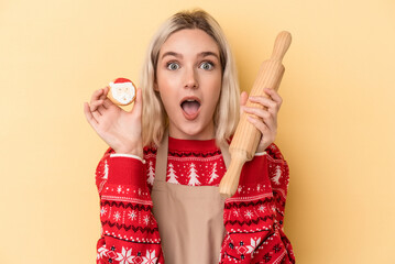 Young caucasian woman holding Christmas cookies isolated on yellow background