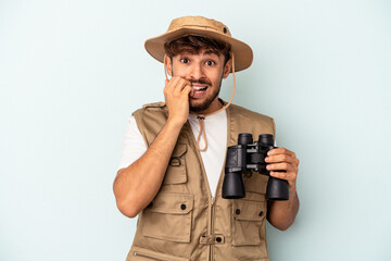 Wall Mural - Young mixed race man holding binoculars isolated on blue background biting fingernails, nervous and very anxious.