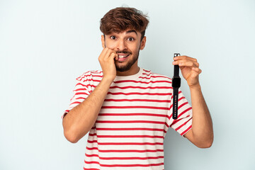 Wall Mural - Young mixed race man holding a wrist watch isolated on blue background biting fingernails, nervous and very anxious.