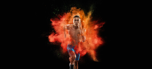 Wall Mural - Creative portrait of young male athlete, sportive man running in explosion of colored neon powder isolated on dark background
