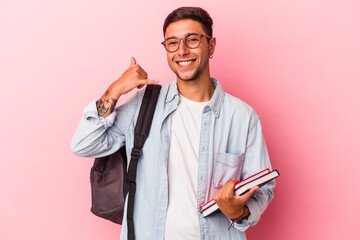 Young caucasian student man holding books isolated on pink background  showing a mobile phone call gesture with fingers.