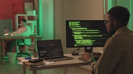 Wall Mural - rear-view stab shot of african-american it specialist hacking software on computer sitting at desk i
