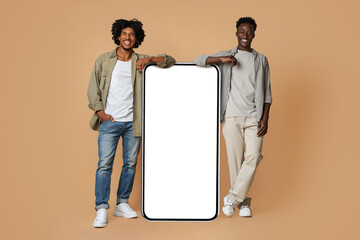 Great App. Two Cheerful Black Friends Leaning At Big Blank Smartphone