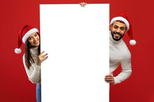 Christmas Advertisement. Happy Arab Couple In Santa Hats Holding White Board, Demonstrating Space For Text Or Design