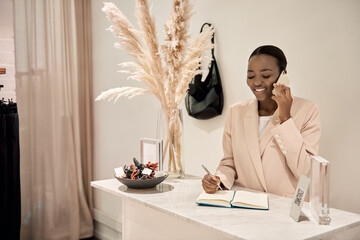 Wall Mural - Smiling African entrepreneur talking on a phone in her boutique