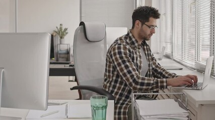 Wall Mural - stab shot of bearded mixed-race programmer in eyeglasses working on laptop and pc sitting at his wor