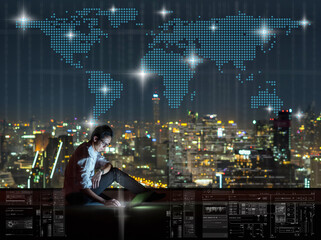 Wall Mural - Asian businessman sitting and using the laptop with Network graphic over the world map dot and cityscape background at night time, Business success and technology concept