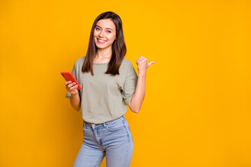 Wall Mural - Photo of young lovely pretty happy positive cheerful smiling girl use phone point thumb copyspace isolated on yellow color background