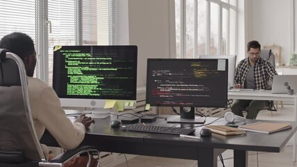 Wall Mural - stab shot of team of programmers sitting at workplaces in front of computer monitors with running pr