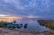 Colorful sunrise on the shore of the lake with fishing boats. Autumn landscape with a lake in the early morning. A bright streak of light on the horizon, dawn.