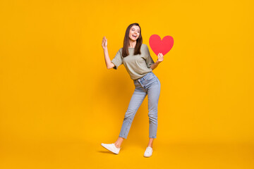 Wall Mural - Full length body size view of lovable cheerful girl holding in hands heart posing isolated over bright yellow color background