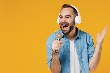 Wall Mural - Young singer fun expressive man 20s wearing blue shirt white t-shirt headphones listen to music sing song in microphone isolated on plain yellow background studio portrait. People lifestyle concept.