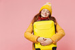 Calm fascinating charming amazing young woman 20s years old wears yellow jacket hat mittens keeping eyes clossed hold hug suitcase bag isolated on plain pastel light pink background studio portrait.